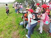 春の多摩川の土手で野鳥を見る1年生児童